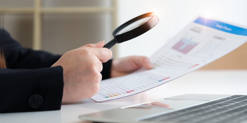 Business woman using magnifying to review balance sheet annual. audit and Check integrity before investment concept.